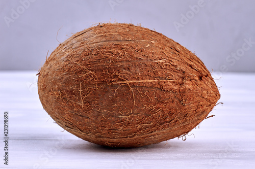 Single whole coconut close up. Brown coconut on light wooden background. Delicious tropical fruit.