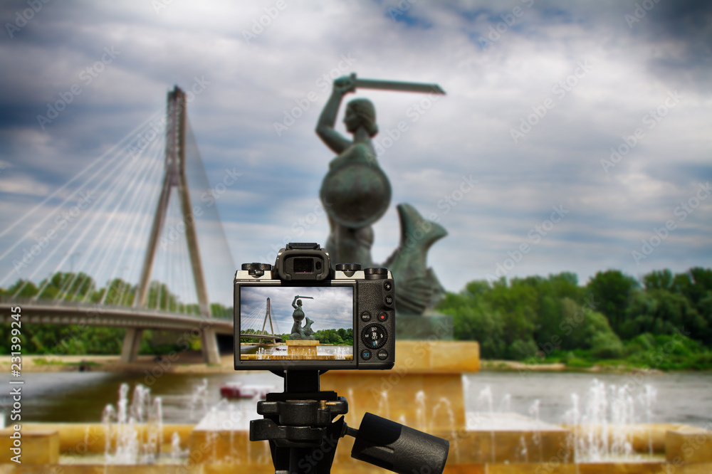 Fototapeta premium Kamera i pomnik Syrenki w Warszawie na tle Mostu Świętokrzyskiego i Wisły