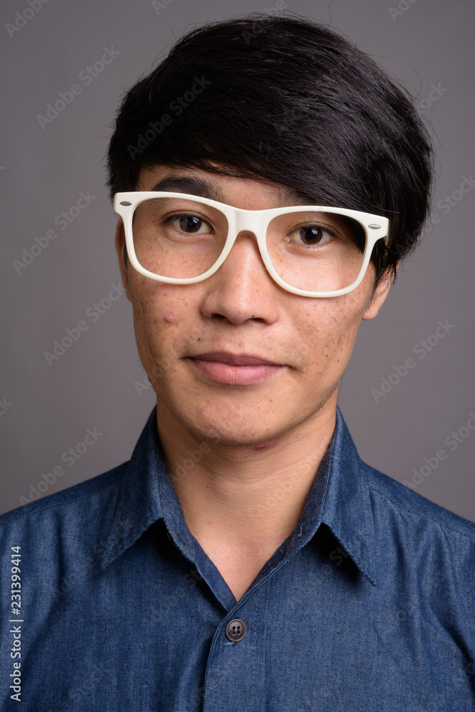 Young Asian man wearing eyeglasses looking smart against gray ba