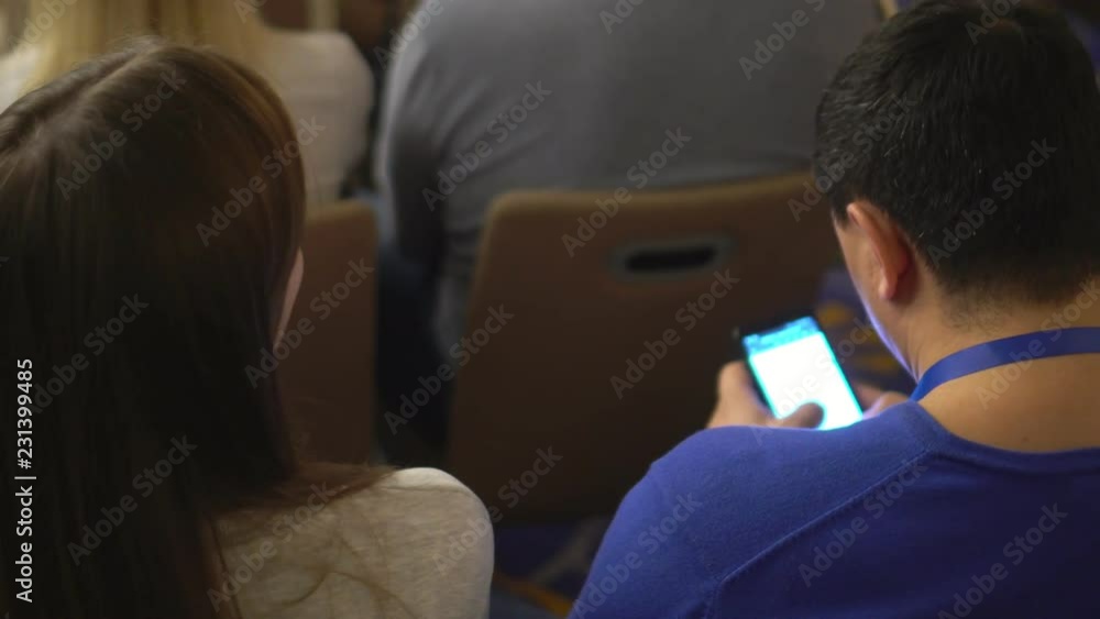 Conference. It is a lot of people. The man works on the smartphone. Hands close up.