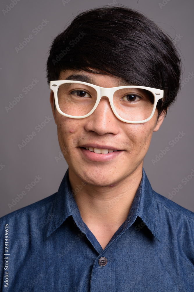 Young Asian man wearing eyeglasses looking smart against gray ba Young Asian man wearing eyeglasses looking smart against gray ba