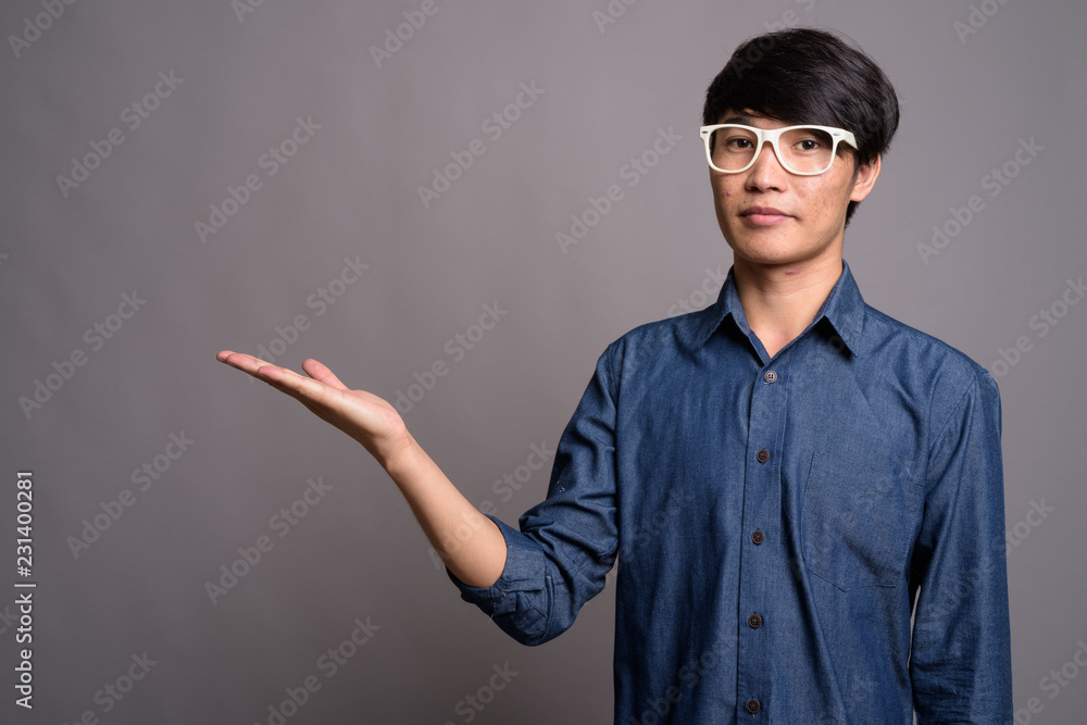 Young Asian man wearing eyeglasses looking smart against gray ba Young Asian man wearing eyeglasses looking smart against gray ba