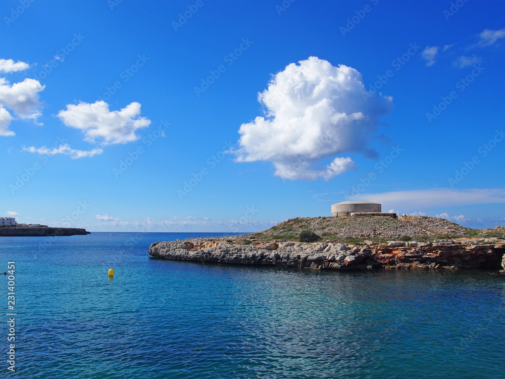 the old british era Torre des Castellar at the edge of the bay in calle santandria near cuitadella with bright blue sea and summer clouds