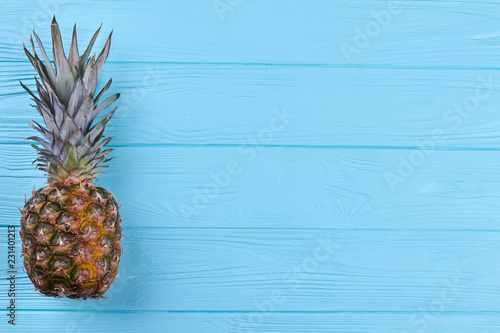 Pineapple with green leaves and copy space. Whole ripe pineapple on blue wooden background and text space. Sweet hawaiian fruit.