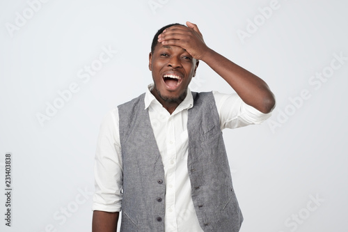 African man remembering funny momen laughing out loud from joy and happiness holding hands on head