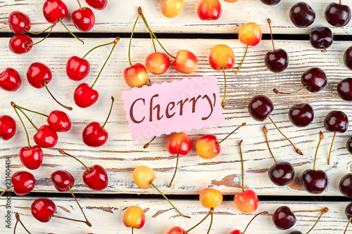 Summer fruits background with ripe cherries. Top view on assortment of organic berries and paper card cherry on wooden background. Summer fruity background.