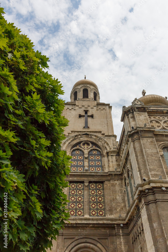 Upward view of Dormition of the Mother of God Cathedral in Varna, Bulgaria, with tree, on the cloudy blue sky day
