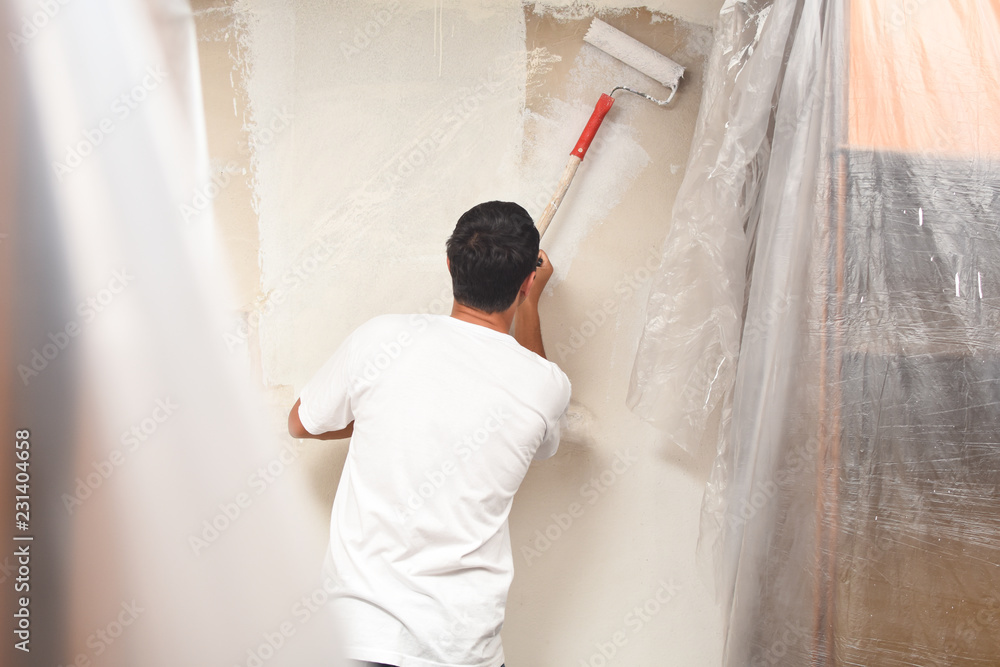 Man painting wall at home with painting roller. Repair home concept. Worker with paint on him after painting dirty walls Man painting wall at home with painting roller. Repair home concept. Worker with paint on him after painting dirty walls