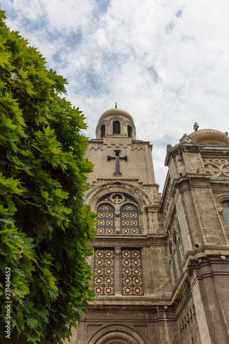 Upward view of Dormition of the Mother of God Cathedral in Varna, Bulgaria, with tree, on the cloudy blue sky day