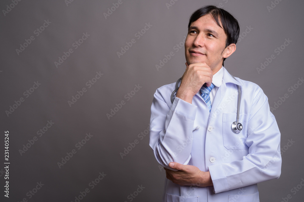Young Asian man doctor against gray background