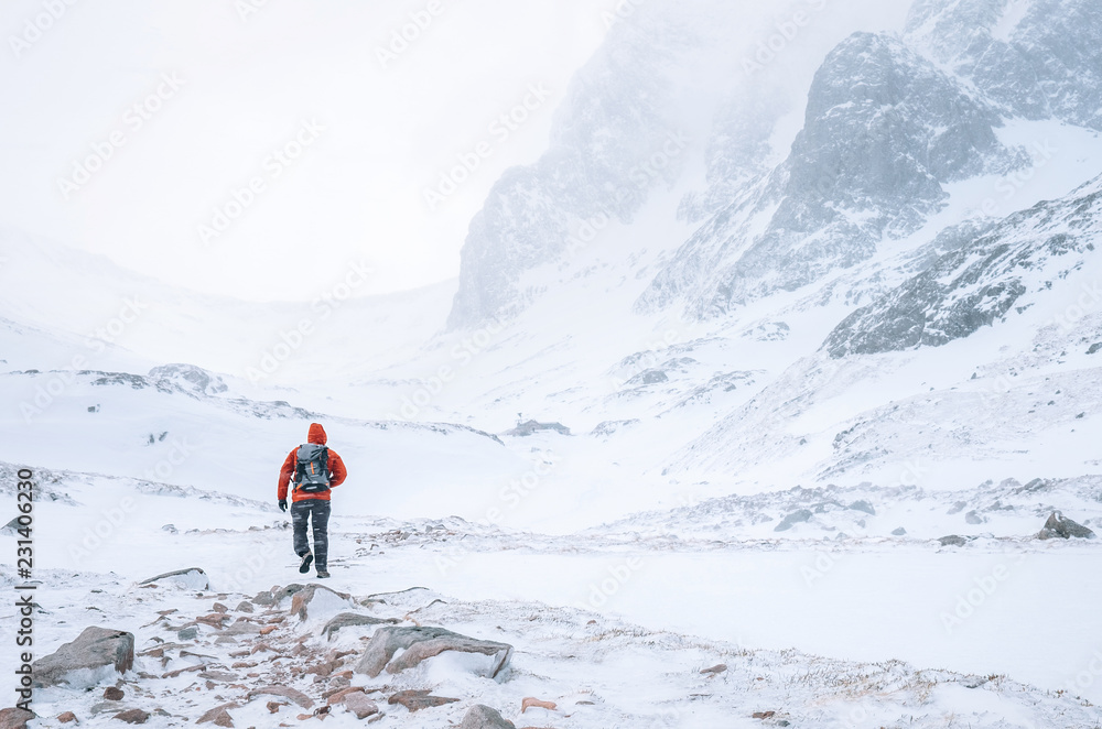 Climber walks alone in high mountains at windy snowy weather