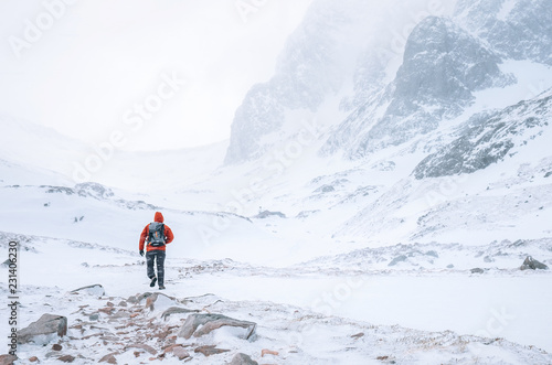 Climber walks alone in high mountains at windy snowy weather
