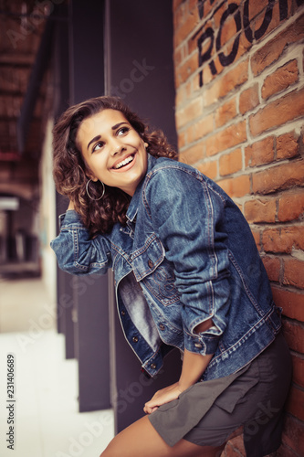 Young latin curly woman while standing on a brick background on a street.
