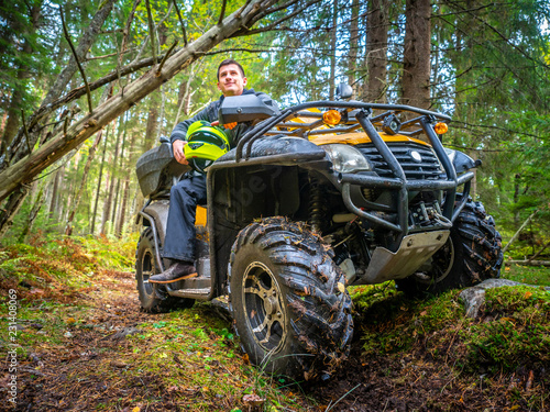 A man travels through the woods on the ATV. A man sits on the ATV in the forest. Off-road. A man travels on a quad.