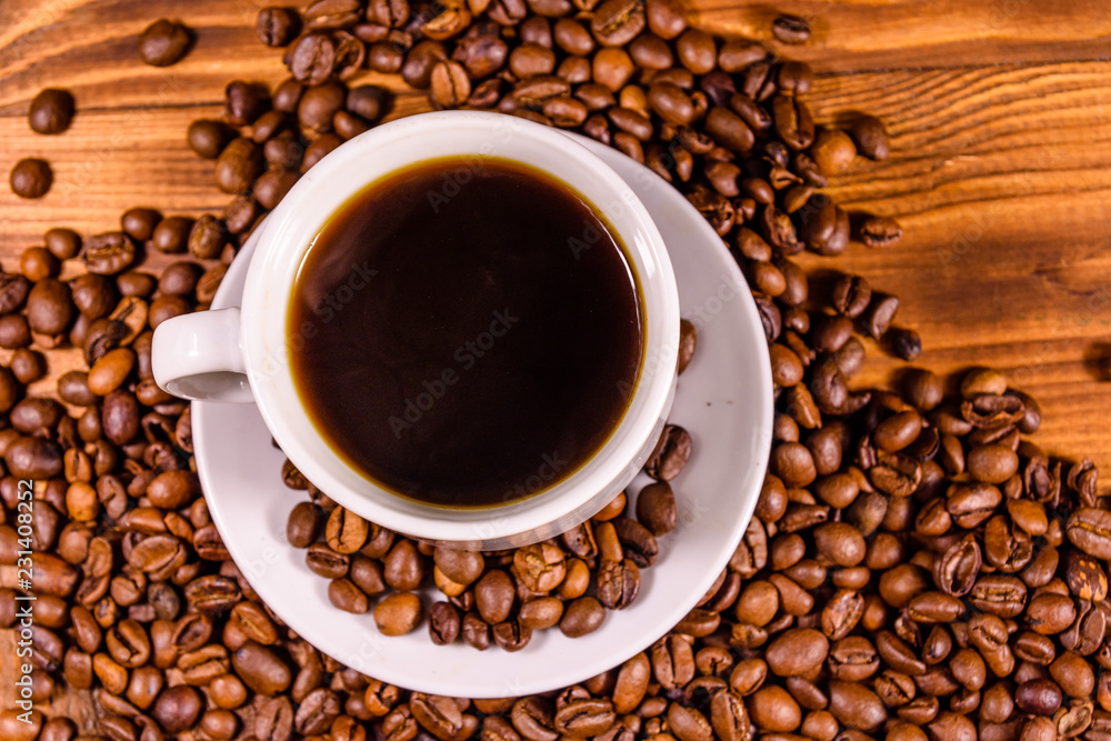 Fototapeta premium Cup of hot coffee and scattered coffee beans on wooden table. Top view