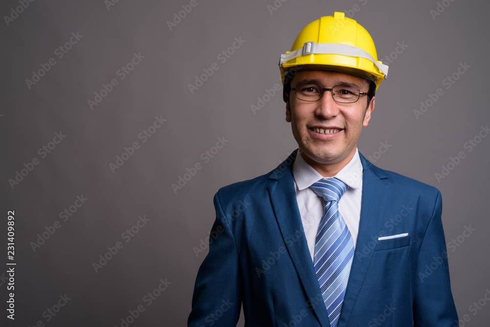 Young Asian businessman wearing hardhat against gray background Young Asian businessman wearing hardhat against gray background