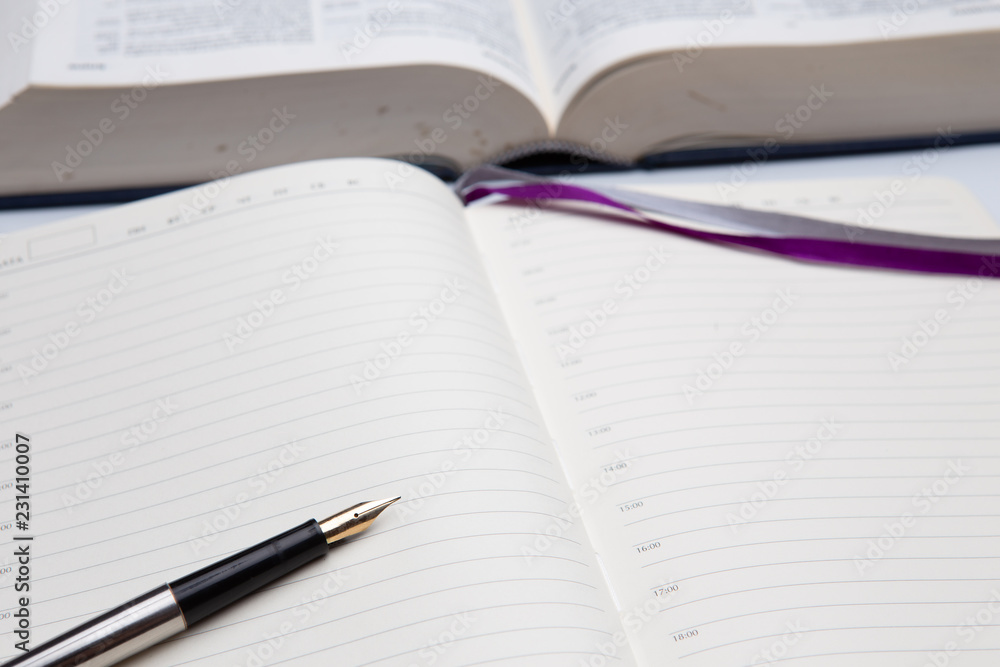 Empty diary or notepad and fountain pen with golden nib closeup, thick opened book in background side view Empty diary or notepad and fountain pen with golden nib closeup, thick opened book in background side view