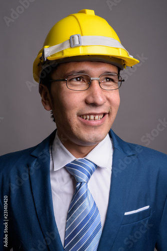 Young Asian businessman wearing hardhat against gray background © Ranta Images