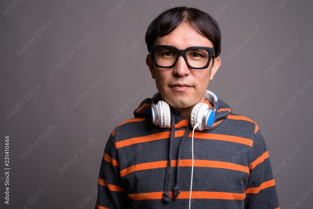Young Asian nerd man wearing hoodie and headphones against gray Young Asian nerd man wearing hoodie and headphones against gray