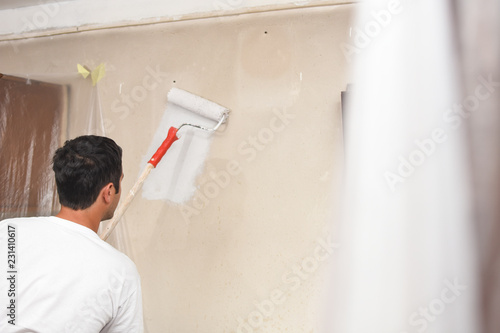 Man painting wall at home with painting roller. Repair home concept. Worker with paint on him after painting dirty walls