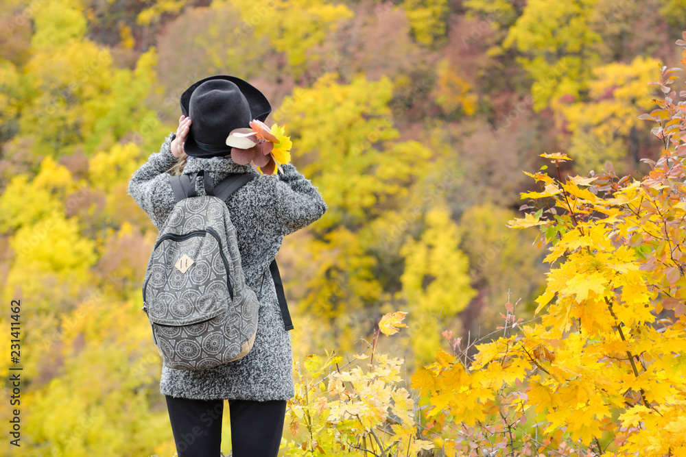 Girl in a hat with a bouquet of yellow leaves. Enjoying of autumn forest. Back view