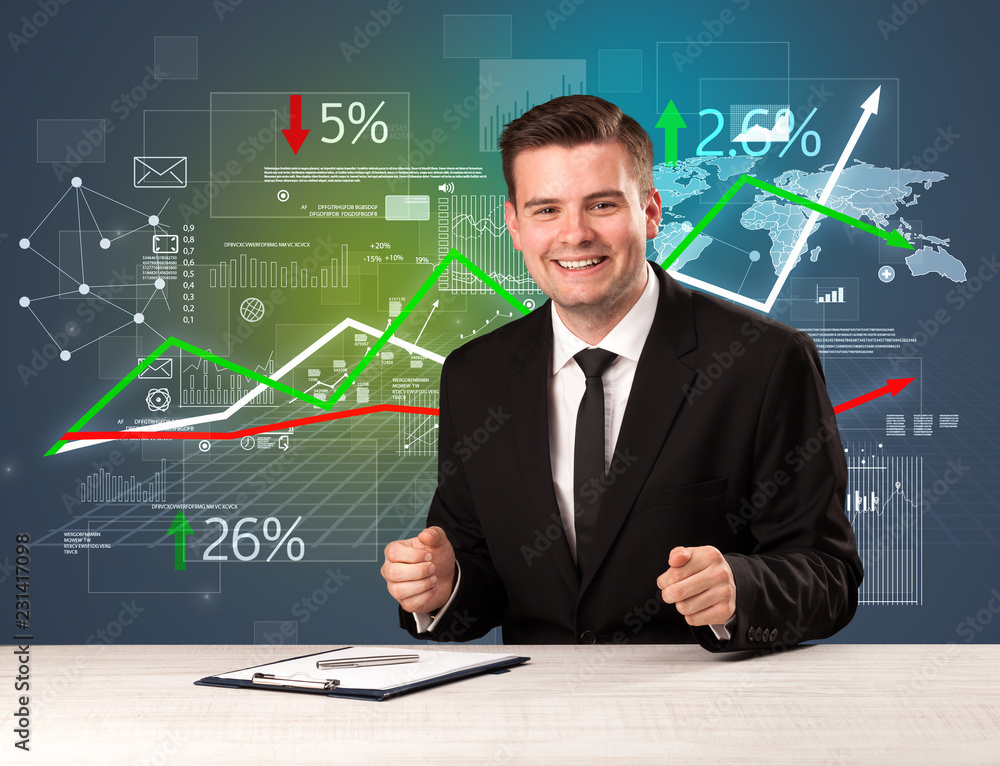 Young handsome businessman sitting at a desk with stocks and progress charts behind him Young handsome businessman sitting at a desk with stocks and progress charts behind him