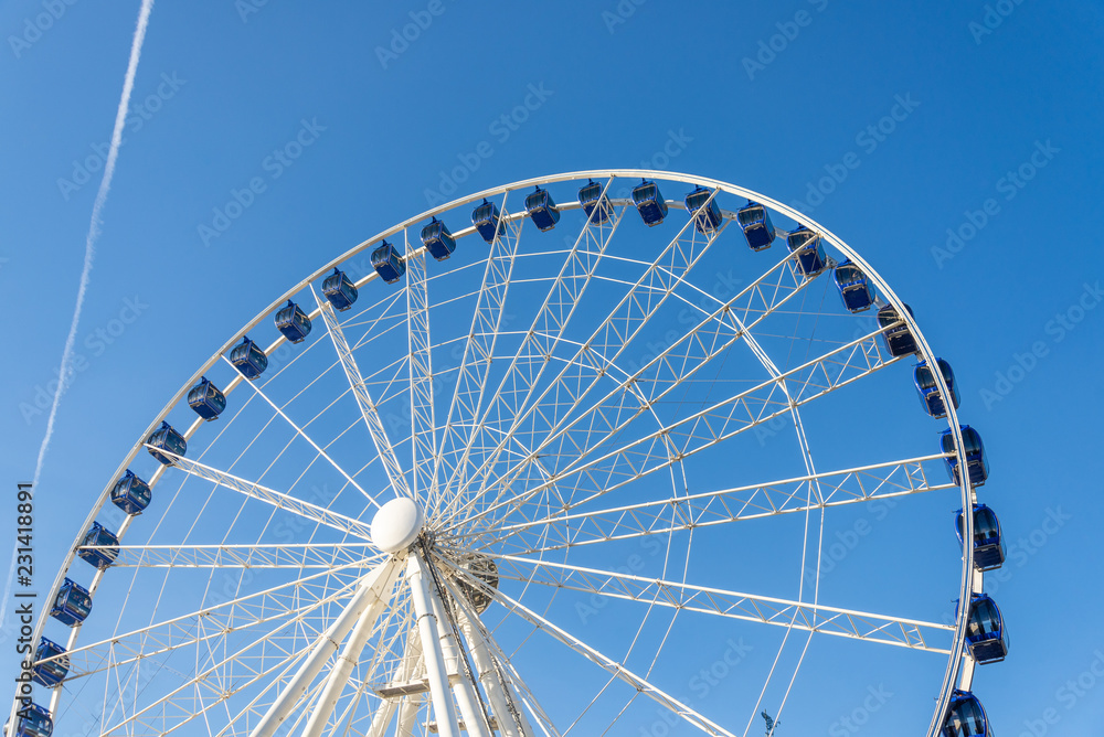 Low angle view of white structure and blue cabin of Ferris wheel with background of clear blue sunny sky.