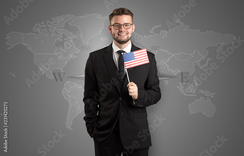 Cheerful businessman standing in front of a map with flag on his hand 