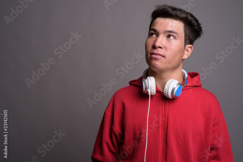Young Asian man wearing headphones against gray background © Ranta Images