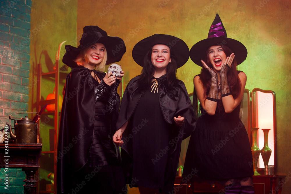 Picture of three witches in black hats in dark room against mirror and rack
