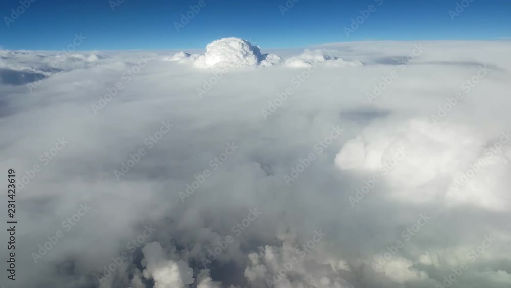 Fairylike view of mountaneous and shaggy white clouds from an airplane window on sunny day in summer.The bright blue sky is above. Fairylike view of mountaneous and shaggy white clouds from an airplane window on sunny day in summer.The bright blue sky is above.