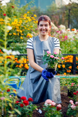 Image of smiling agronomist brunette holding pink roses in garden