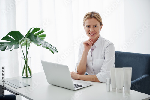 Canvas Print Waist up portrait of beautician in white lab coat working on computer at her office