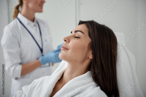Side view portrait of attractive woman in white bathrobe lying with closed eyes during medical procedure