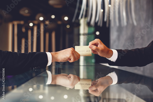 Laconic image of young man in dark suit giving his gold card to the professional receptionist