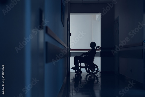 Lady is sitting in wheelchair in hallway. She is using it for travelling through hospital. Copy space in left side
