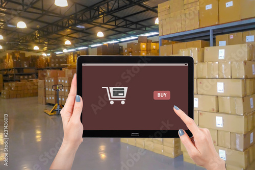 Shopping online concept, Hand using mock up computer tablet on warehouse background, with copy space