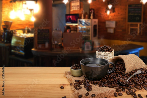 Hot cup of coffee and beans with burlap sack on the wooden table, at the coffee shop background with copy space