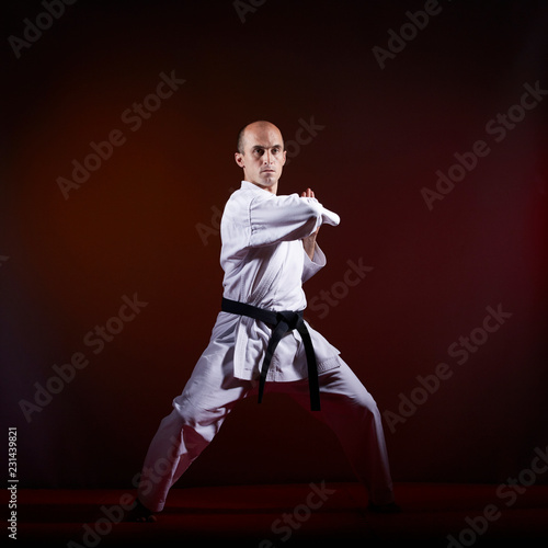 Adult athlete in karategi trains formal karate exercises on a dark background