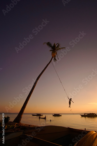 Silhouette of indentify Bajau Kids playing a swing under coconut tree during sunset at Maiga Island, Sempoerna.