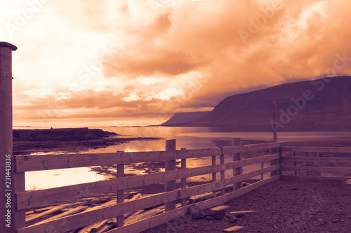 Iceland landscape and wooden sheep fold - coast line  fjords  ocean bay  hills  mountains and clouds. Selective focus. Sunset sky.