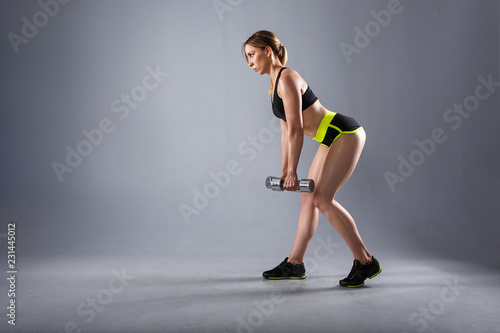 Strong young sportswoman trains with dumbbells in a sport suit. Concept of pumping muscle and nutrition. Copyspace