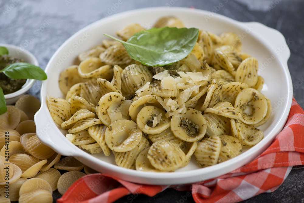 Close-up of a white plate with orecchiette pasta served with green basil pesto and parmesan cheese, horizontal shot Close-up of a white plate with orecchiette pasta served with green basil pesto and parmesan cheese, horizontal shot