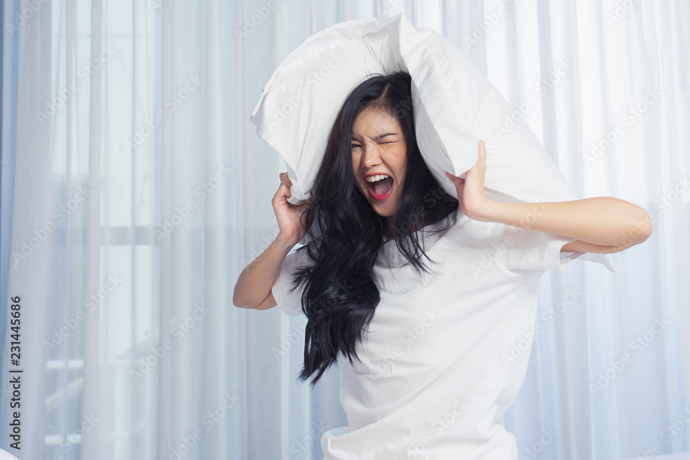 Young woman lying in bed suffering from sound covering head and ears with pillow making unpleasant face. Do not oversleep again Young woman lying in bed suffering from sound covering head and ears with pillow making unpleasant face. Do not oversleep again