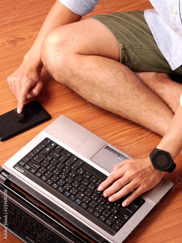 Closeup of a man sitting typing on keybord of his laptop and his smartphone simultaneously.