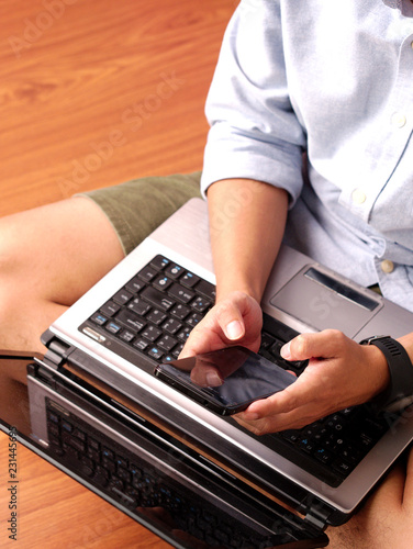 Wallpaper Mural Closeup of a man sitting typing on his mobilephone with his laptop on his lap. Torontodigital.ca