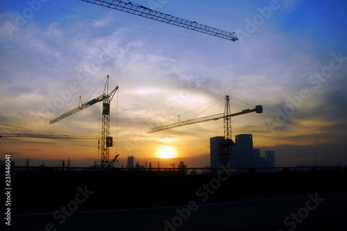 Silhouette of crane and building construction site in the city at sunrise.