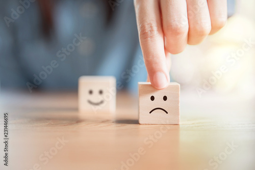 Close up customer hand choose sad face and blurred smiley face icon on wood cube, Service rating, satisfaction concept. photo