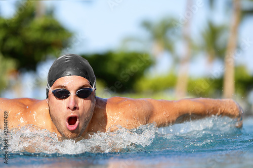Swim training man swimmer butterfly stroke at outdoor swimming pool.. Competitive male sport athlete swimmer wearing swimming goggles and cap. Fitness sport lifestyle.