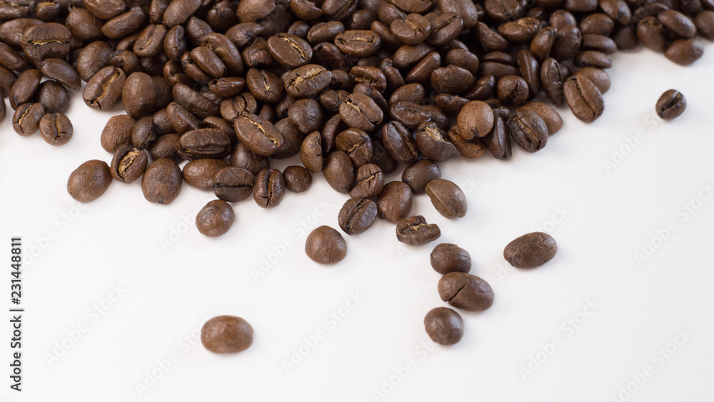 Brown, roasted coffee beans are shown up close and loosely spread out on a plain, white surface. Brown, roasted coffee beans are shown up close and loosely spread out on a plain, white surface.